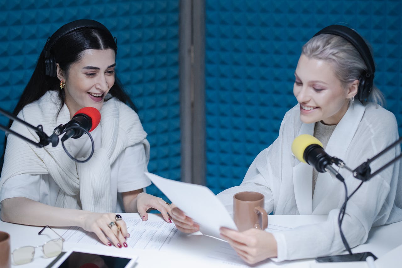 Two women recording a lively podcast episode in a professional studio setting.