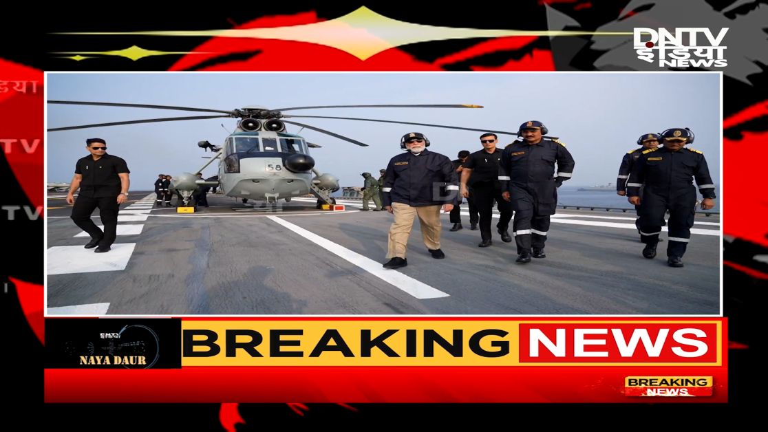 प्रधानमंत्री नरेंद्र मोदी INS विक्रांत पर नौसेना की शक्ति प्रदर्शन के दौरान सलामी देते हुए, पृष्ठभूमि में युद्धपोत और नौसैनिक टुकड़ियां।